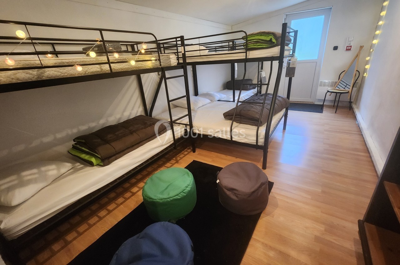 Chambre avec lits superposés, matelas préparés, poufs colorés et lumière naturelle entrant par une porte vitrée.