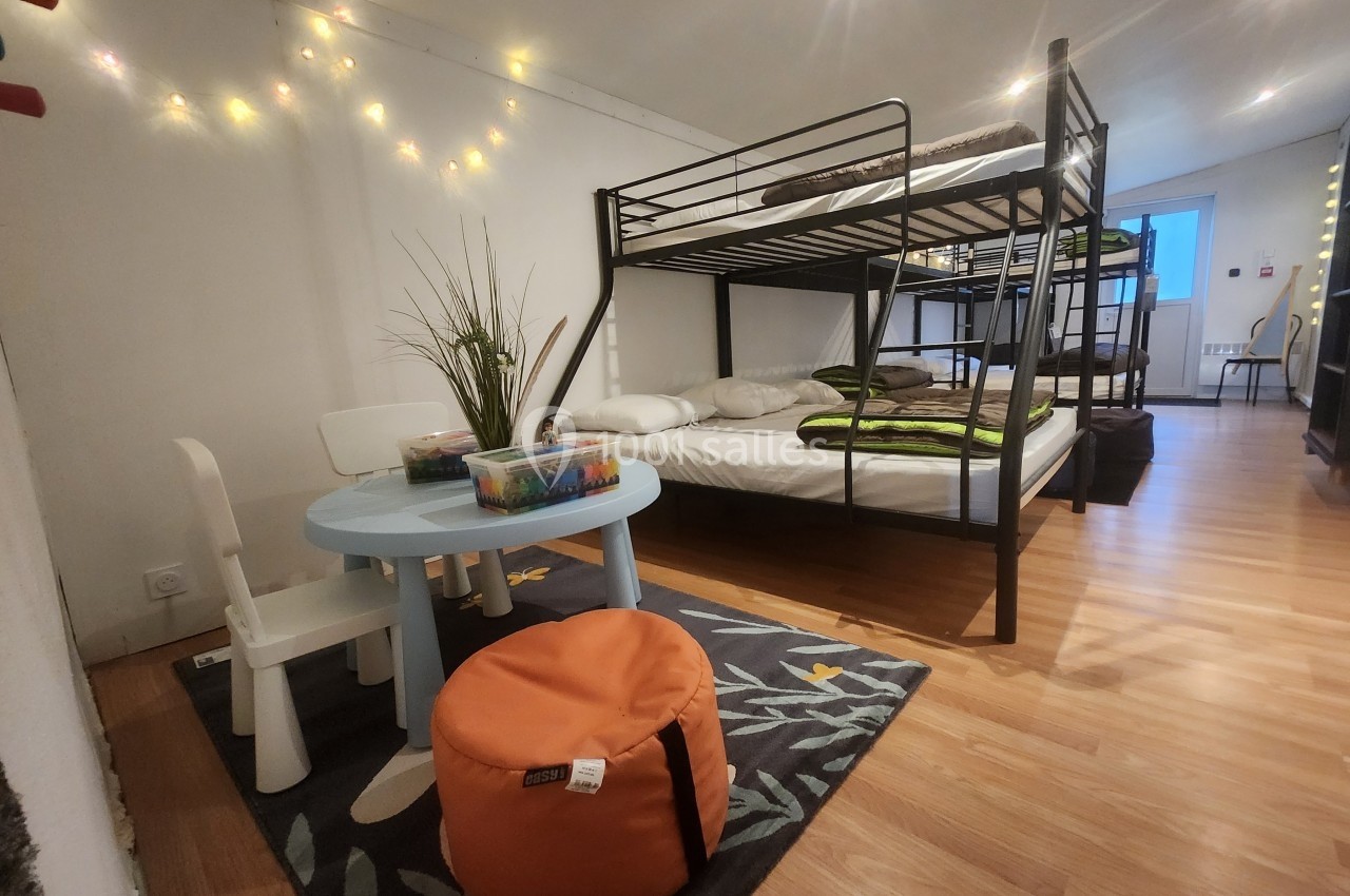 Chambre avec lits superposés, lit double, table basse avec chaises pour enfants et décoration lumineuse.