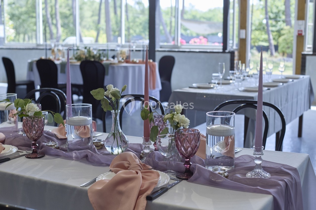 Table dressée avec nappes violettes, verres colorés, bougies et décorations florales dans une salle lumineuse.