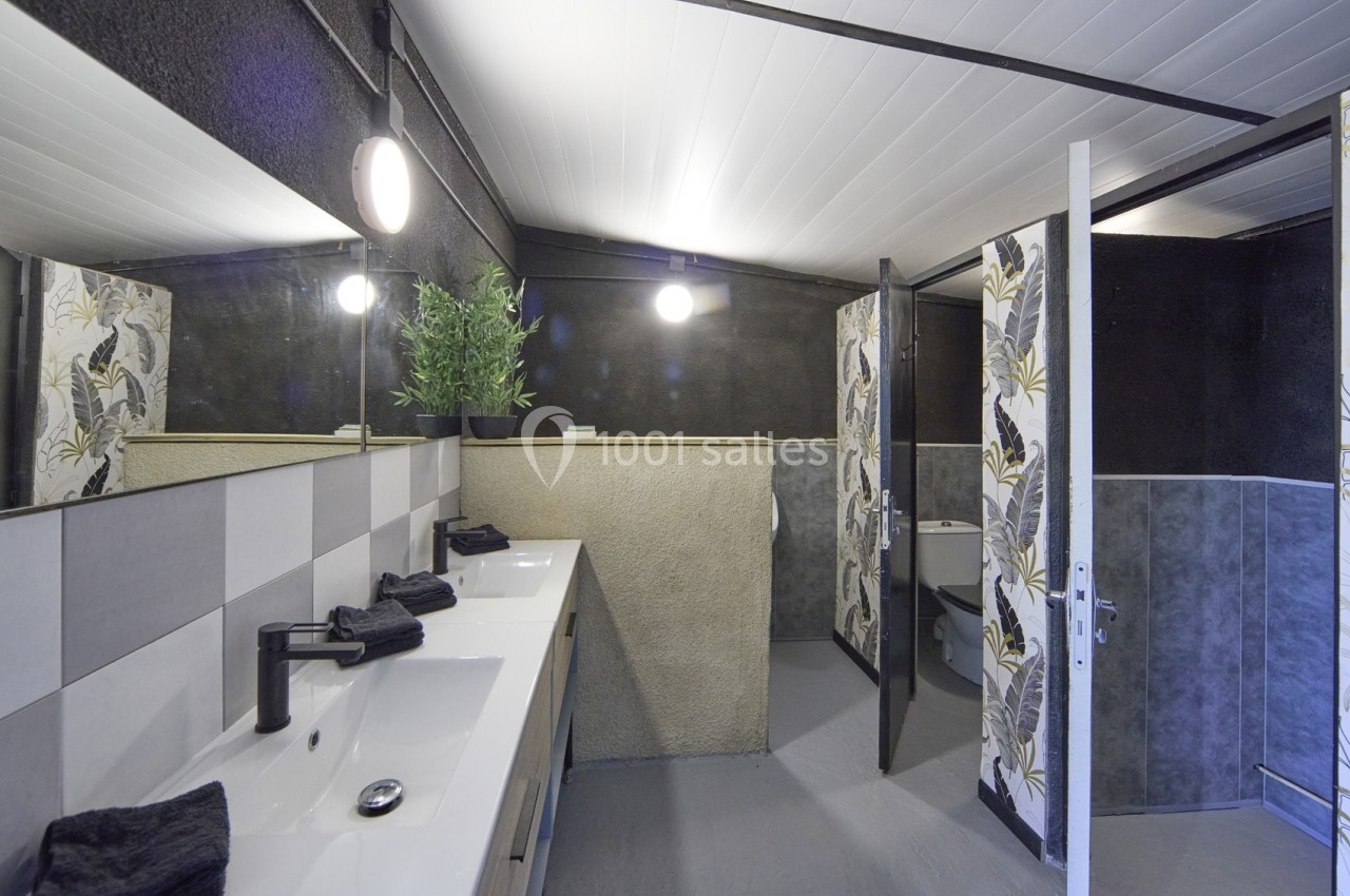 Salle de bain moderne avec double vasque, robinets noirs, miroir, éclairage rond et cabine de douche en arrière-plan.