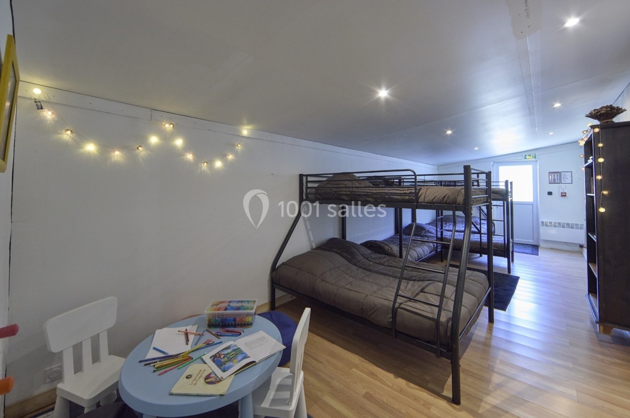 Chambre avec lits superposés, table basse avec chaises pour enfants, guirlande lumineuse et sol en parquet.