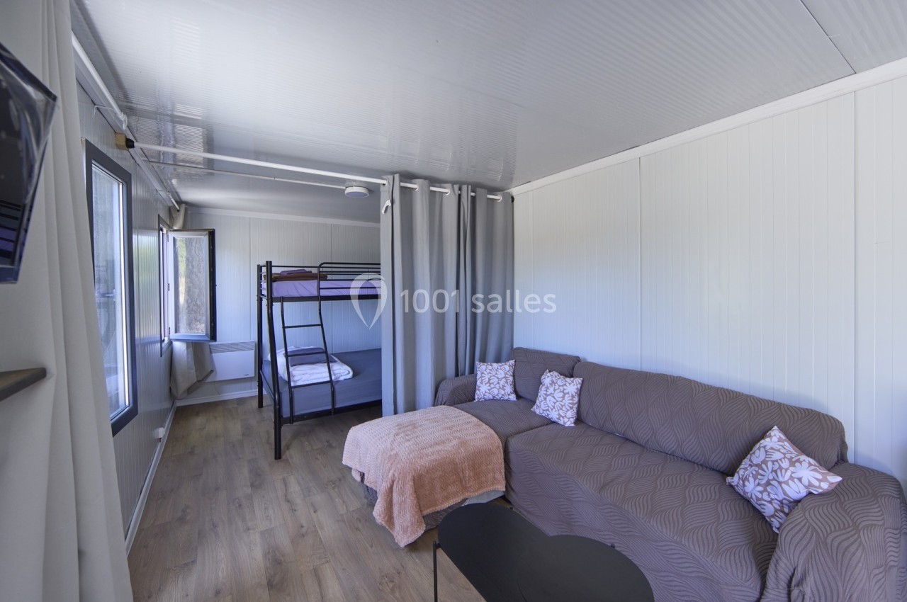 Intérieur d'une pièce lumineuse avec lits superposés, canapé, table basse et parquet en bois clair.