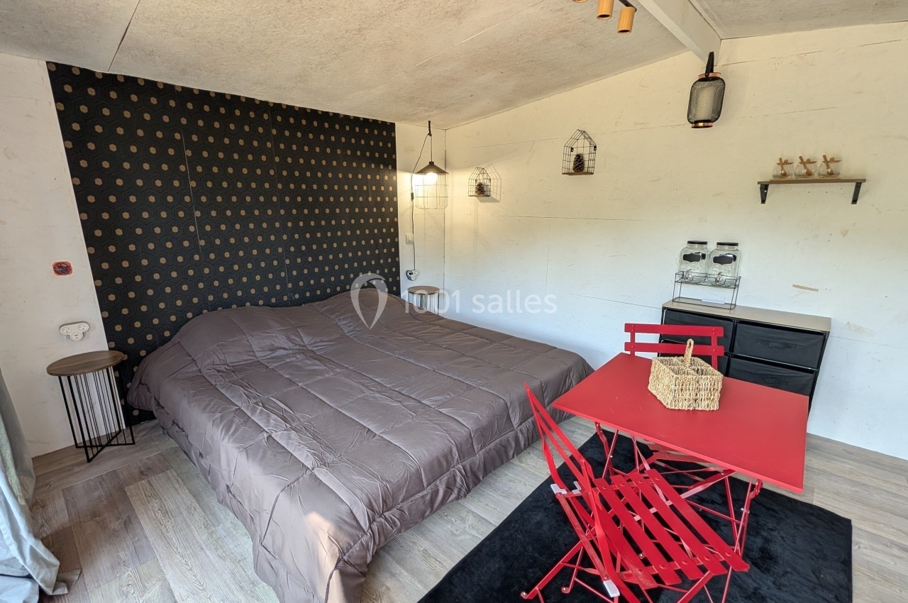 Chambre avec lit double, mur décoré de motifs, table rouge avec chaises pliantes et mobilier minimaliste.