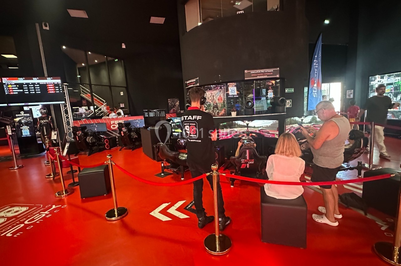 Des visiteurs observent des simulateurs de course automobile dans un espace intérieur avec un sol rouge et des écrans.