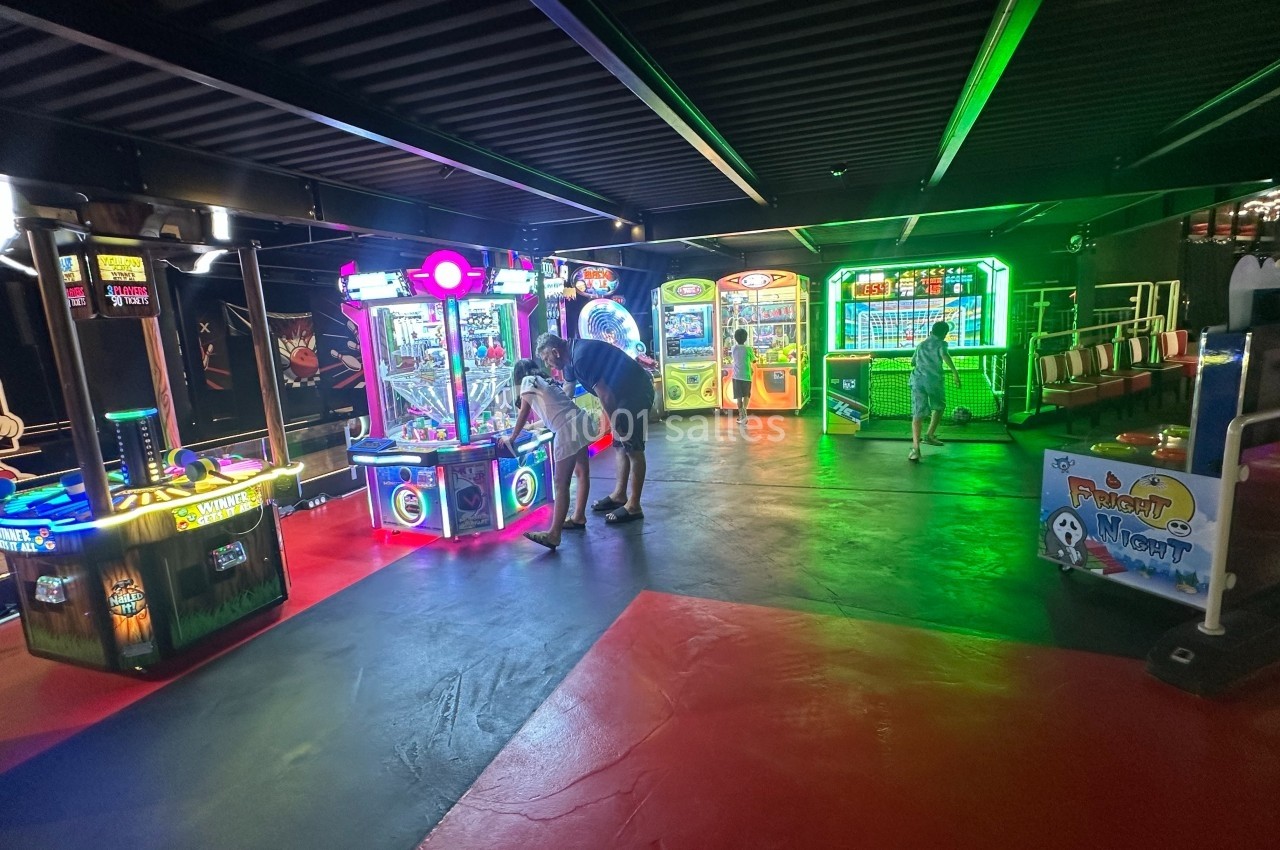 Salle d'arcade colorée avec diverses machines de jeux interactifs et quelques personnes en train de jouer.