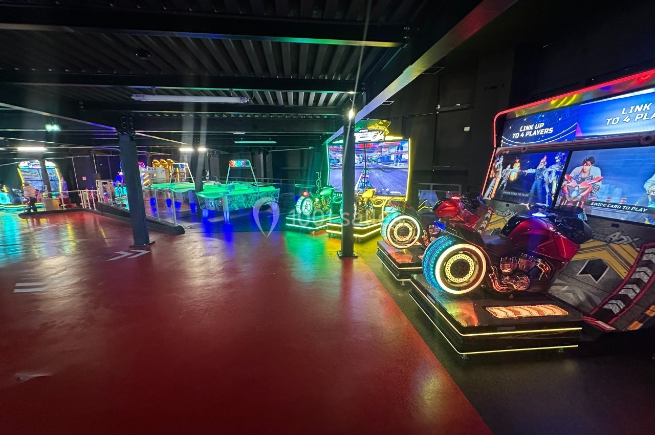 Salle d'arcade avec jeux interactifs lumineux, dont des simulateurs de moto et une table de hockey sur air.