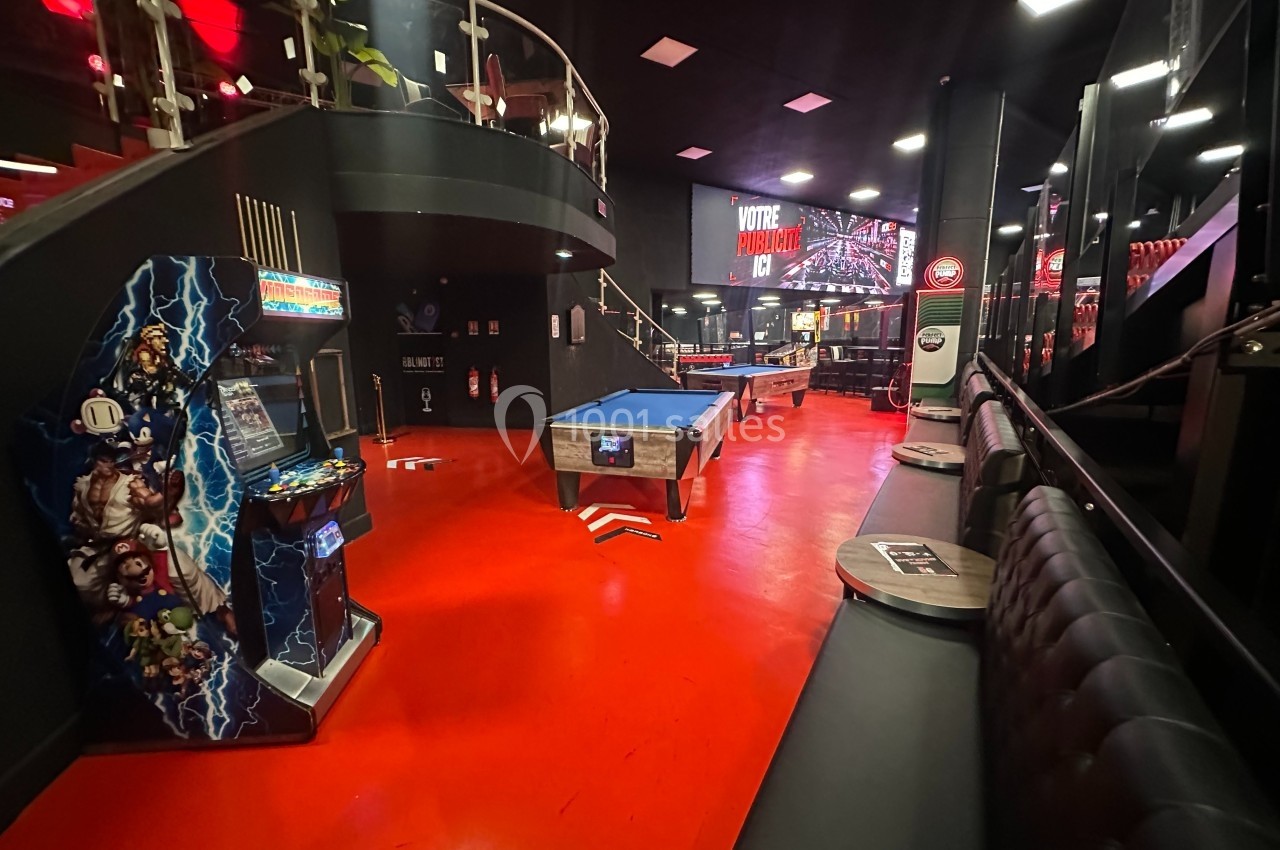 Salle de loisirs avec billard, borne d'arcade et banquettes, éclairée par des lumières rouges et blanches.