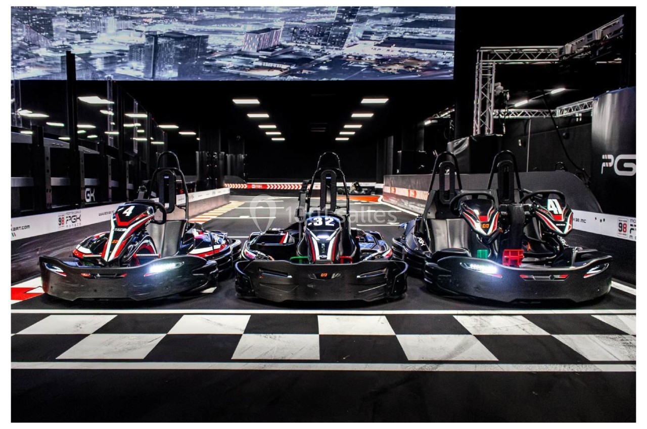 Trois karts électriques alignés sur une piste intérieure, prêts pour une course, avec un décor urbain en arrière-plan.