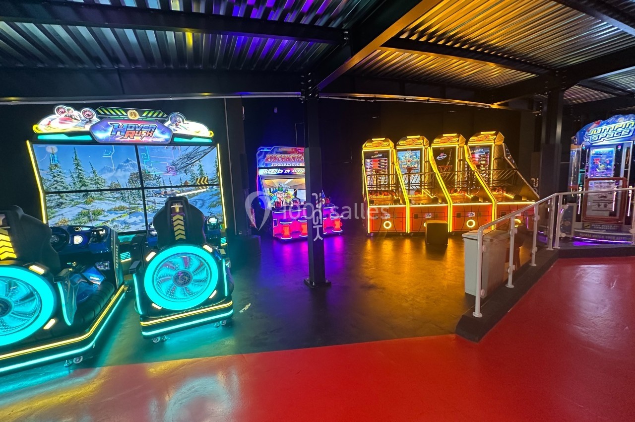 Salle d'arcade avec plusieurs bornes de jeux lumineuses alignées sous un éclairage coloré.