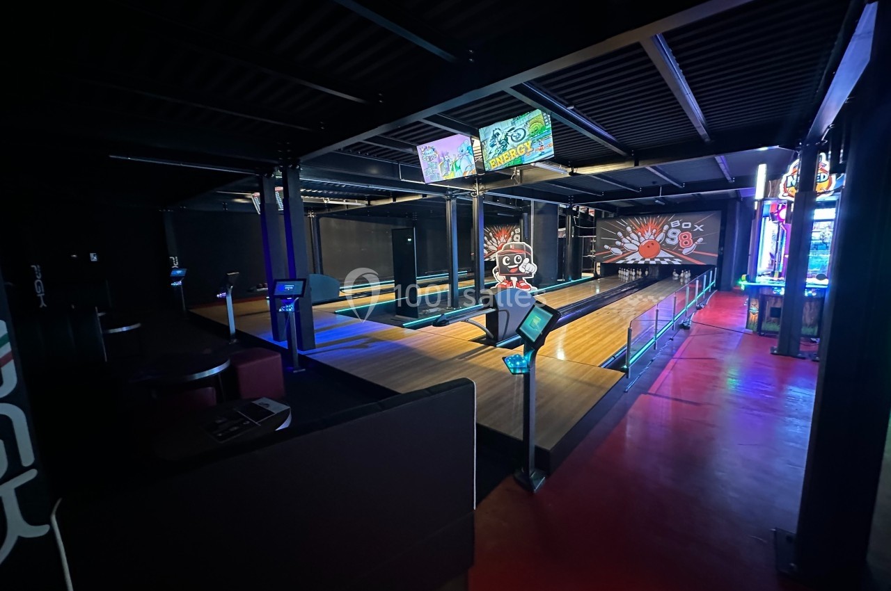 Pistes de bowling éclairées avec des néons, entourées de sièges et d'écrans interactifs dans une ambiance sombre.