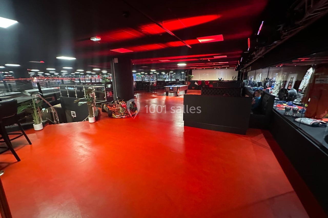Salle intérieure avec sol rouge, éclairage tamisé, mobilier noir et plantes disposées près des murs.