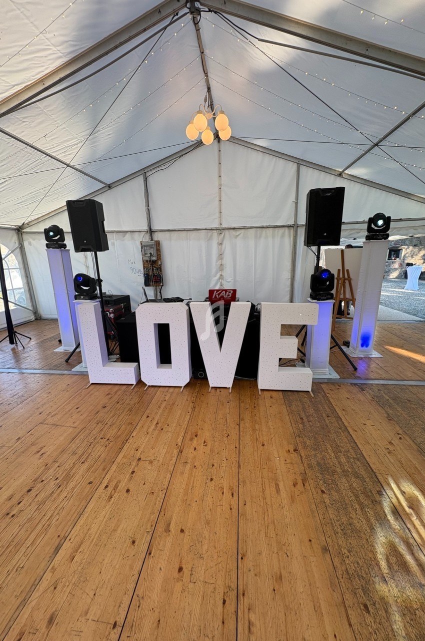Lettres géantes formant le mot ’LOVE’ dans une tente décorée avec des lumières et un espace pour DJ.