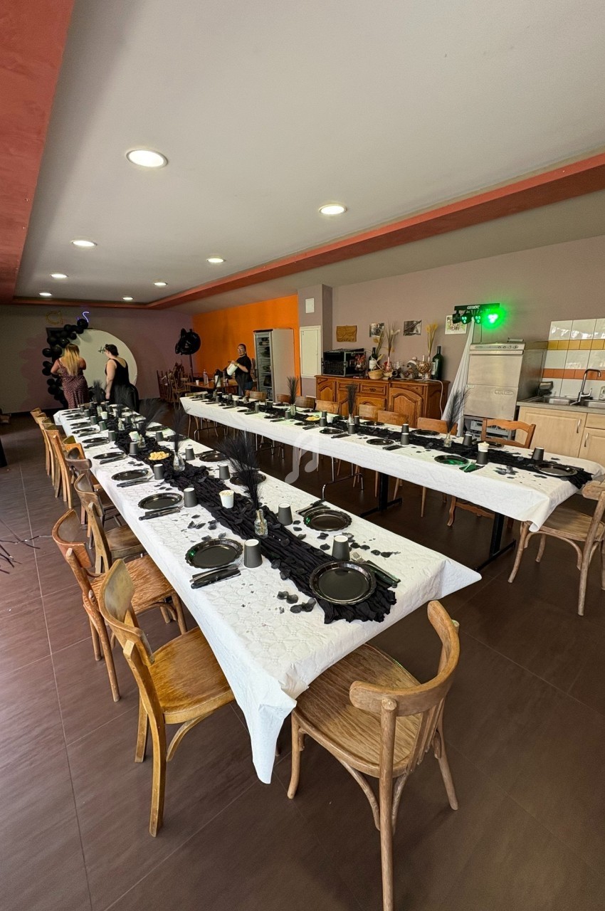 Salle décorée avec deux longues tables dressées avec vaisselle noire et blanche, prête pour un événement festif.