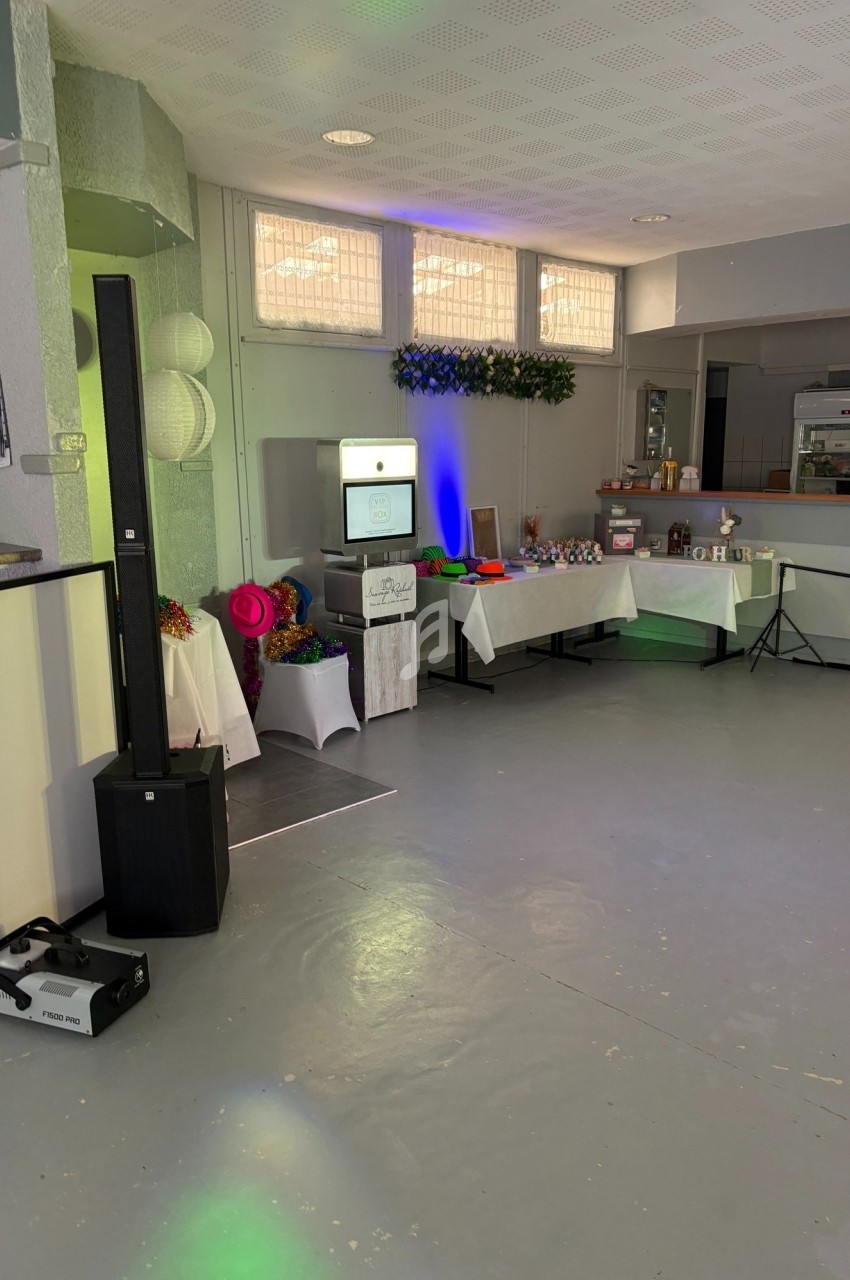 Salle décorée avec une borne photo, tables garnies d’accessoires colorés et un buffet en arrière-plan.