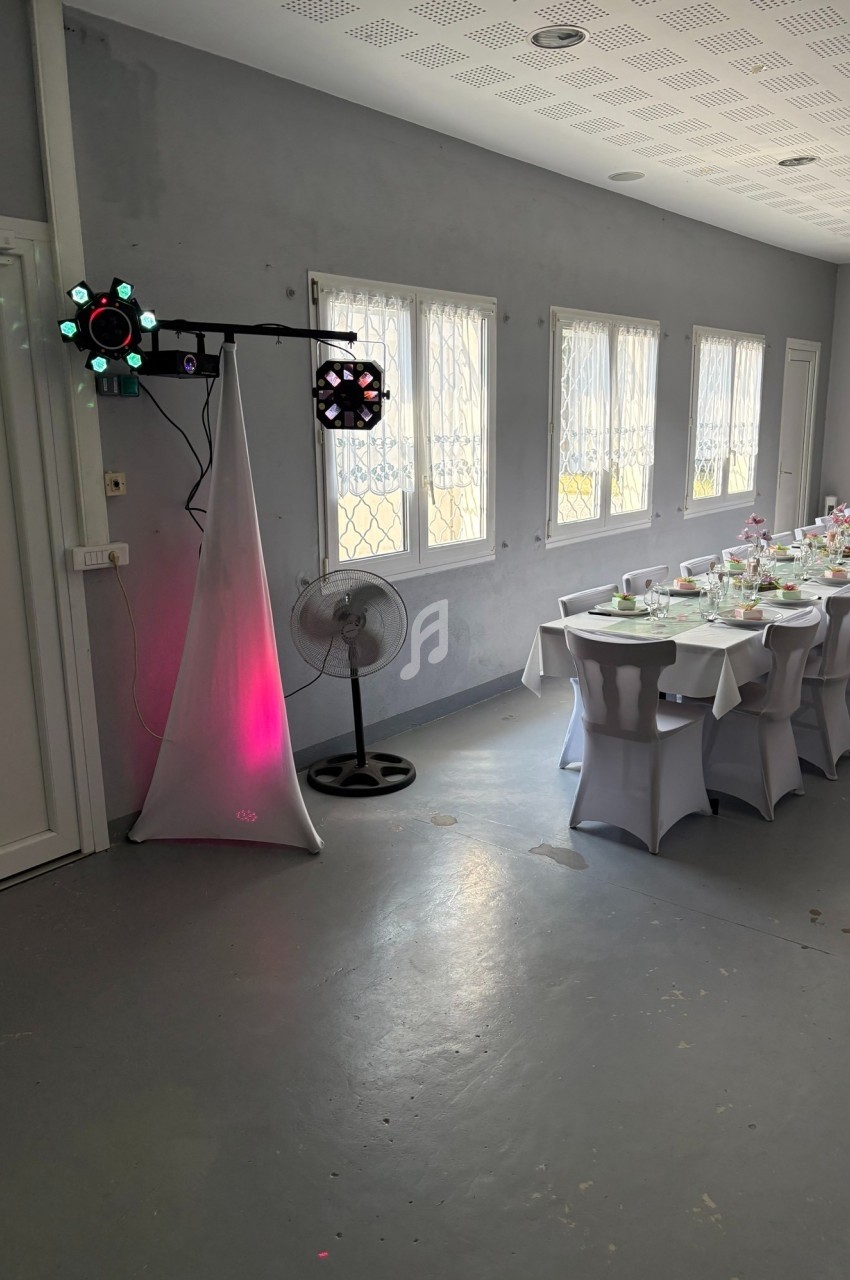 Salle décorée pour un événement, avec une table dressée et un éclairage d'ambiance près d'un ventilateur.
