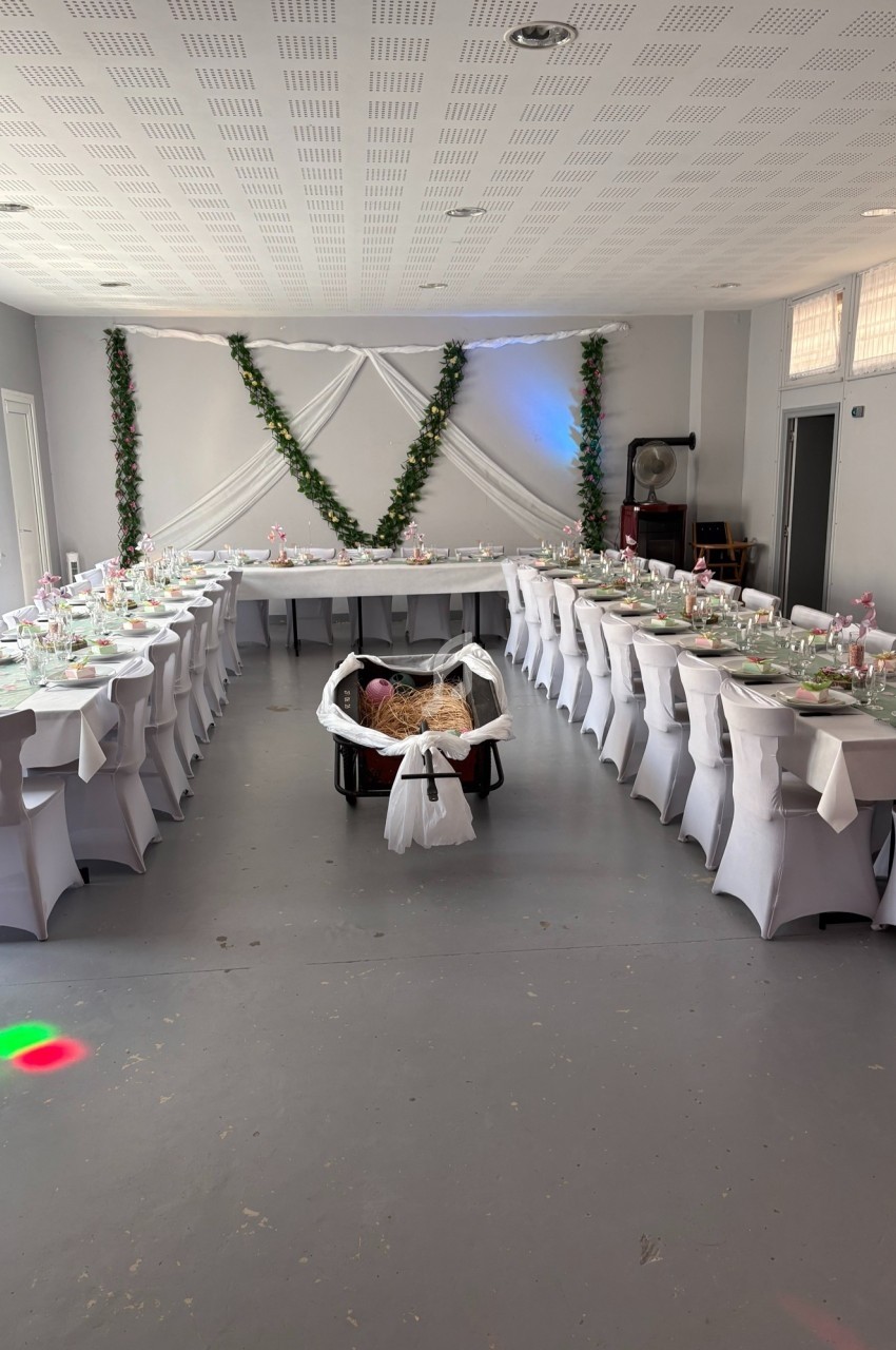 Salle décorée pour un événement avec tables dressées en U, nappes blanches et guirlandes de feuillage au mur.