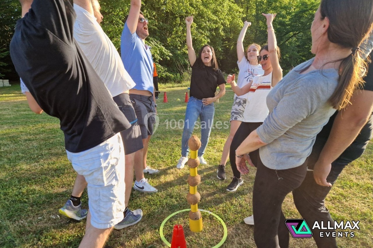 Un groupe de personnes célèbre autour d'un jeu d'adresse avec des noix de coco empilées sur une pelouse.