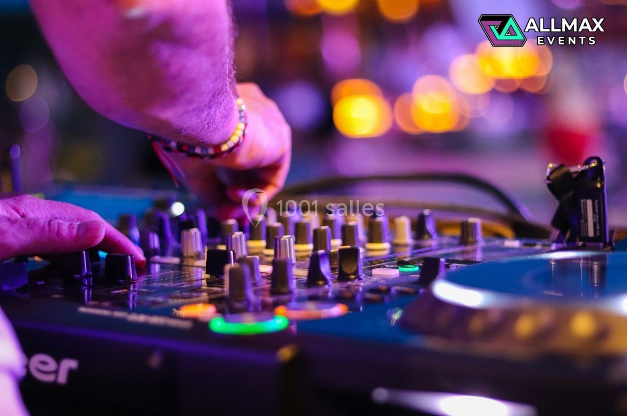 Un DJ ajuste les commandes d'une table de mixage lors d'un événement lumineux en soirée.
