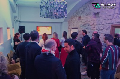 Salle comble avec des participants levant les mains, un intervenant flou en arrière-plan sur une scène.