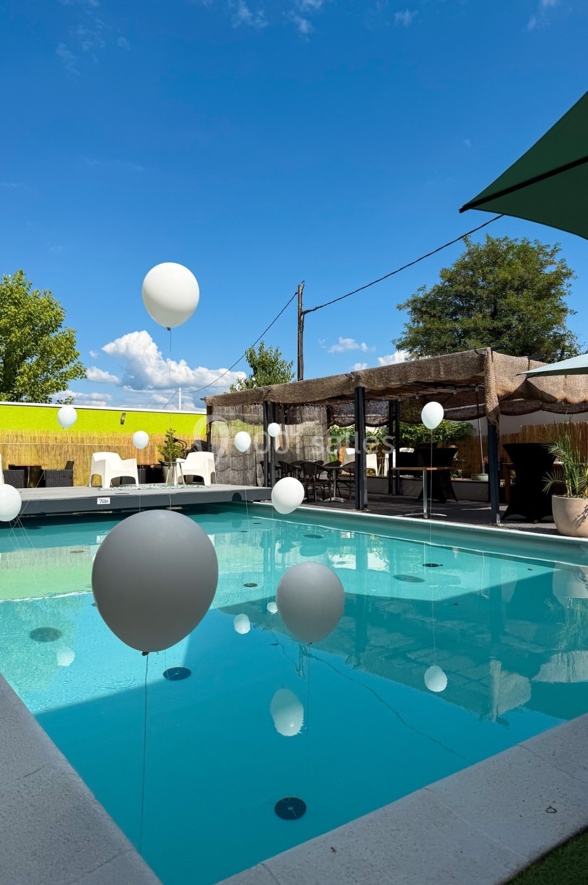Piscine extérieure entourée de chaises et de parasols, décorée de ballons blancs flottant au-dessus de l'eau.