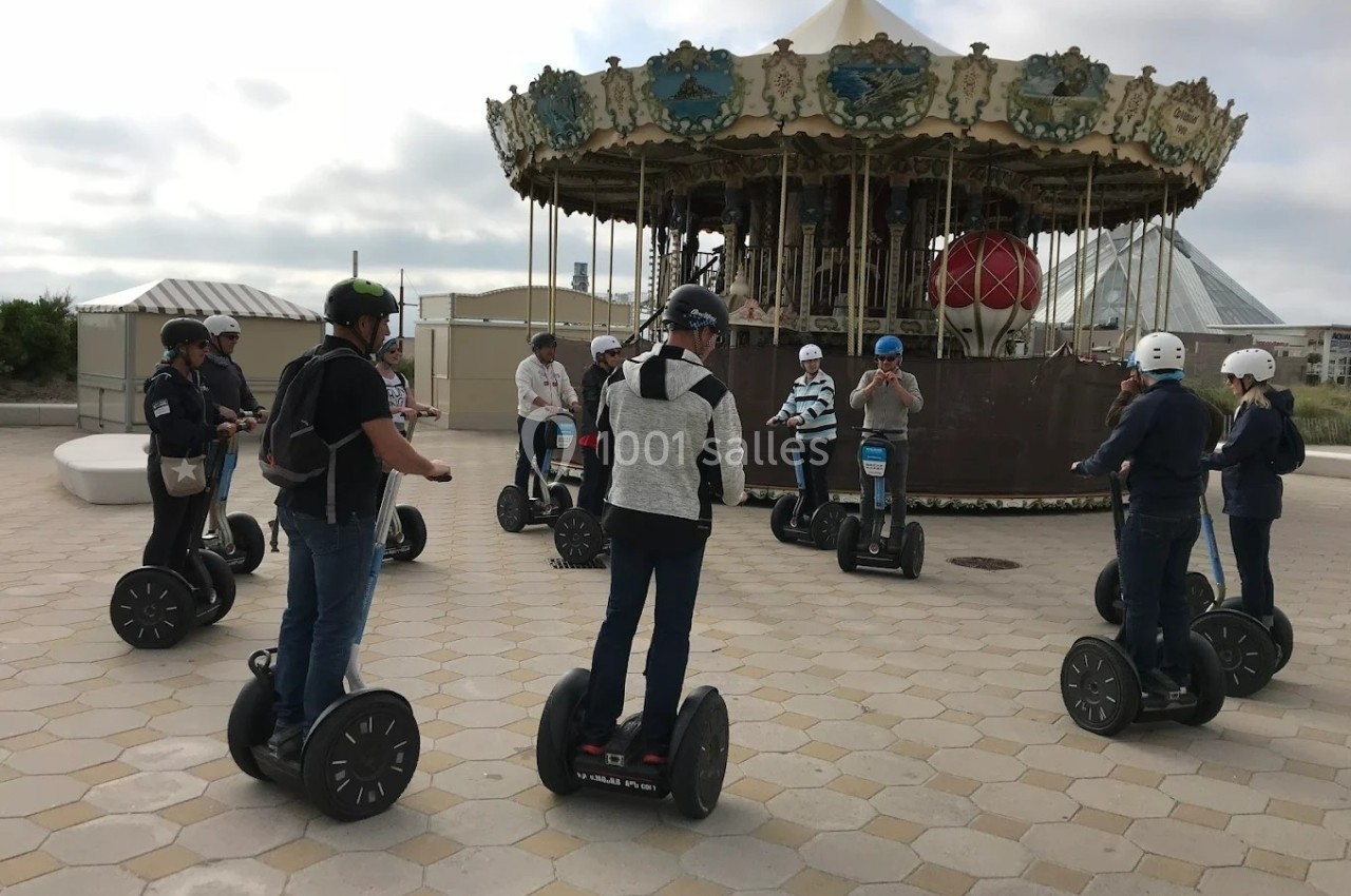Groupe de personnes en segways rassemblées devant un carrousel sur une place pavée.
