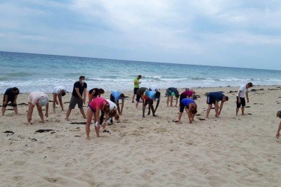 Un groupe de personnes s'étire sur une plage de sable près de la mer sous un ciel nuageux.