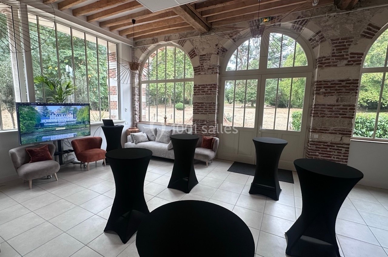 Salle lumineuse avec grandes fenêtres, murs en briques, mobilier moderne et vue sur un jardin arboré.