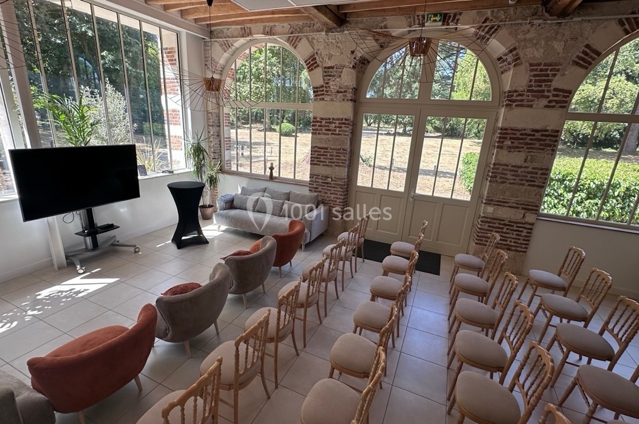 Salle lumineuse avec grandes fenêtres, aménagée pour un événement avec des chaises disposées face à un écran.
