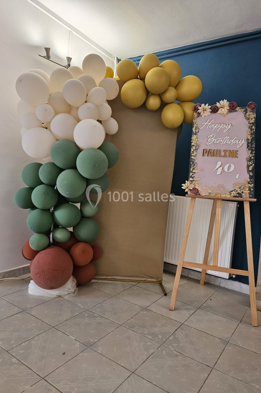 Décoration d'anniversaire avec arche de ballons verts, blancs et dorés, et panneau sur chevalet indiquant ’Happy Birthday…