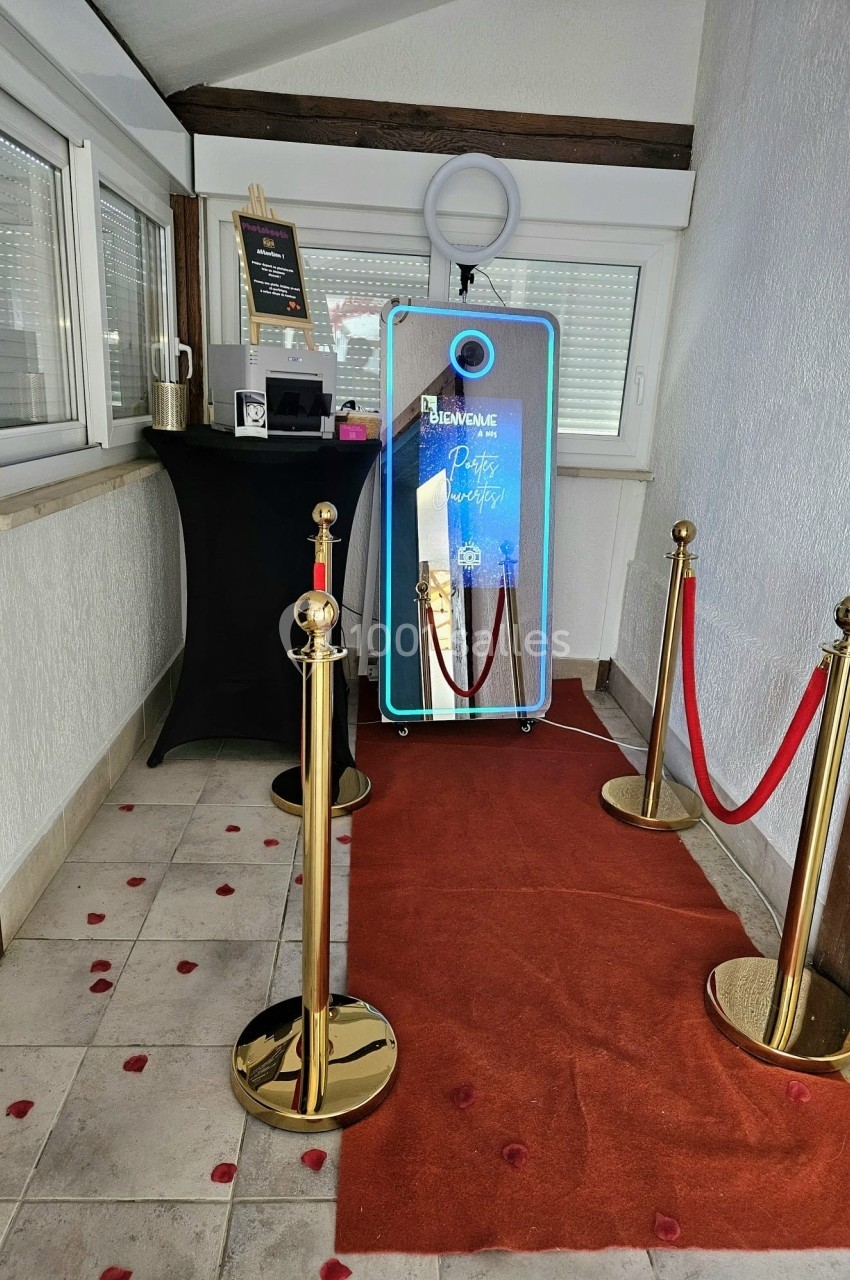Miroir interactif lumineux entouré de poteaux dorés et tapis rouge dans un coin de pièce décoré.