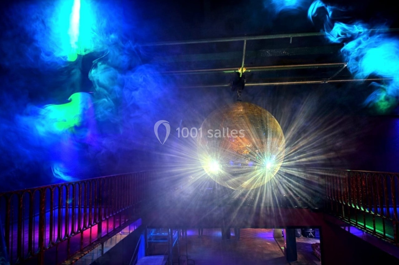 Une boule disco dorée suspendue reflète des faisceaux lumineux colorés dans une salle obscure avec de la fumée.