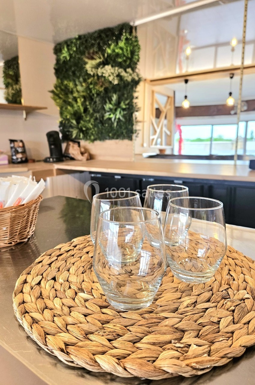 Quatre verres transparents posés sur un dessous de plat en osier, dans une cuisine moderne avec mur végétal en arrière-plan.