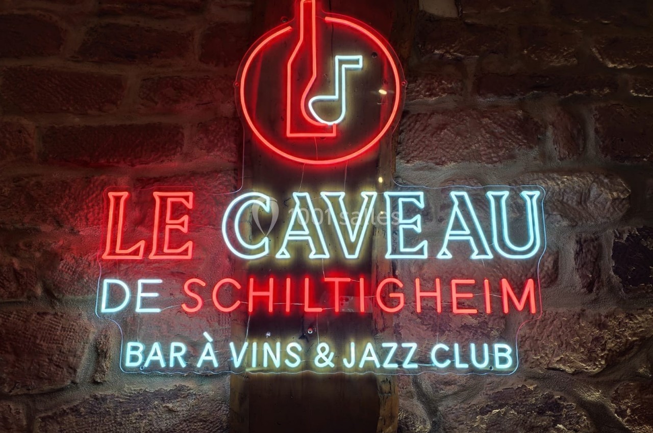Enseigne lumineuse en néon indiquant ’Le Caveau de Schiltigheim, bar à vins & jazz club’ sur un mur en pierre.
