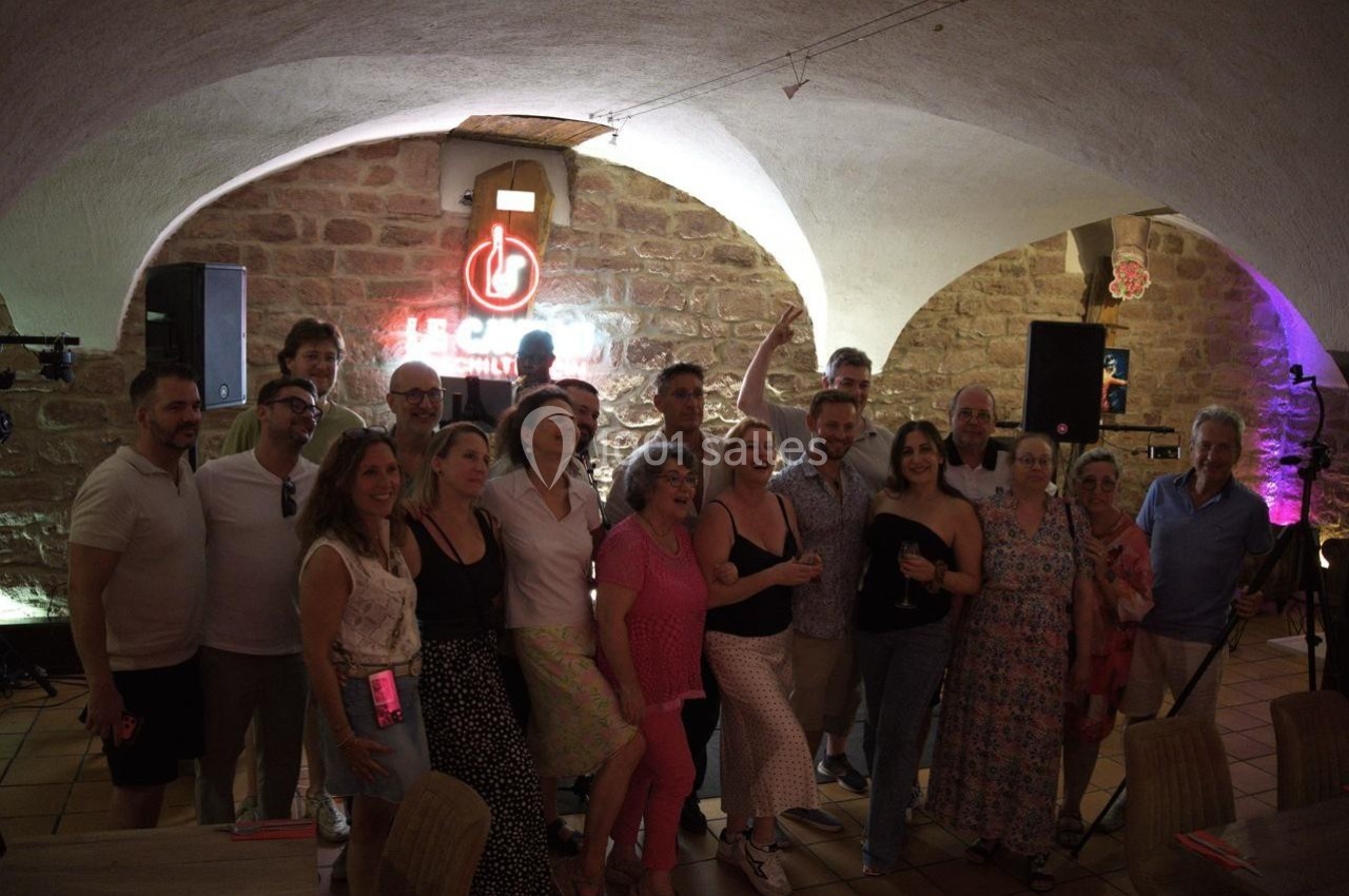 Un groupe de personnes pose ensemble dans une salle voûtée en pierre, éclairée par des lumières colorées.