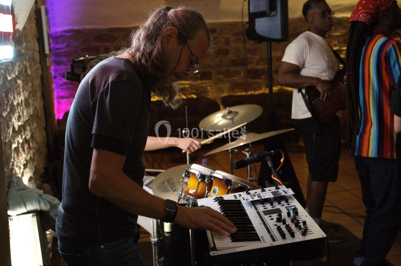Un musicien joue du clavier électronique lors d'un concert avec un batteur et un bassiste en arrière-plan.
