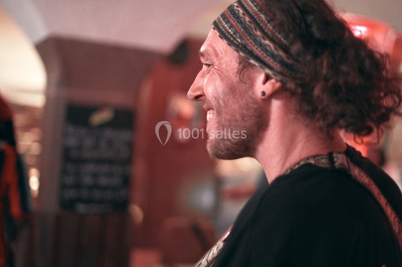 Homme souriant de profil, portant un bandeau coloré, dans un environnement intérieur lumineux et flou.