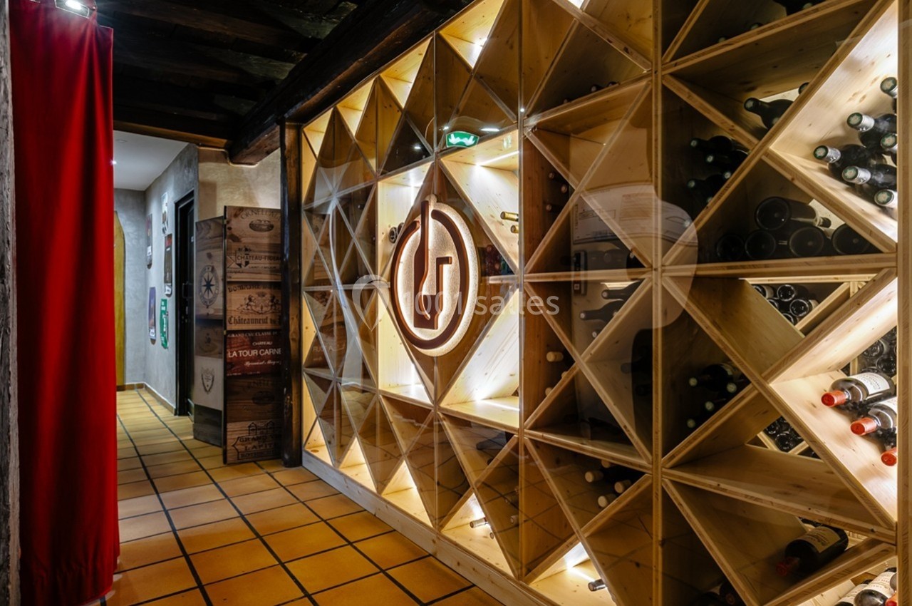 Mur de casiers en bois contenant des bouteilles de vin, éclairé par des lumières intégrées, dans un couloir carrelé.