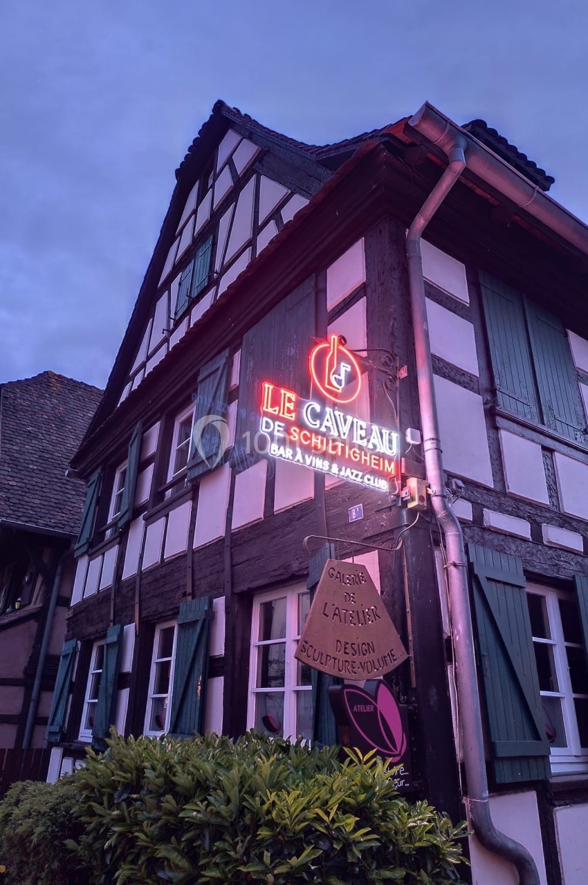 Façade d'une maison à colombages avec enseignes lumineuses indiquant un bar à vins et une galerie d'art.