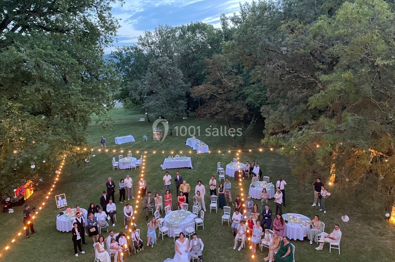 Groupe de personnes rassemblées en extérieur pour une réception, entourées de tables et de guirlandes lumineuses.
