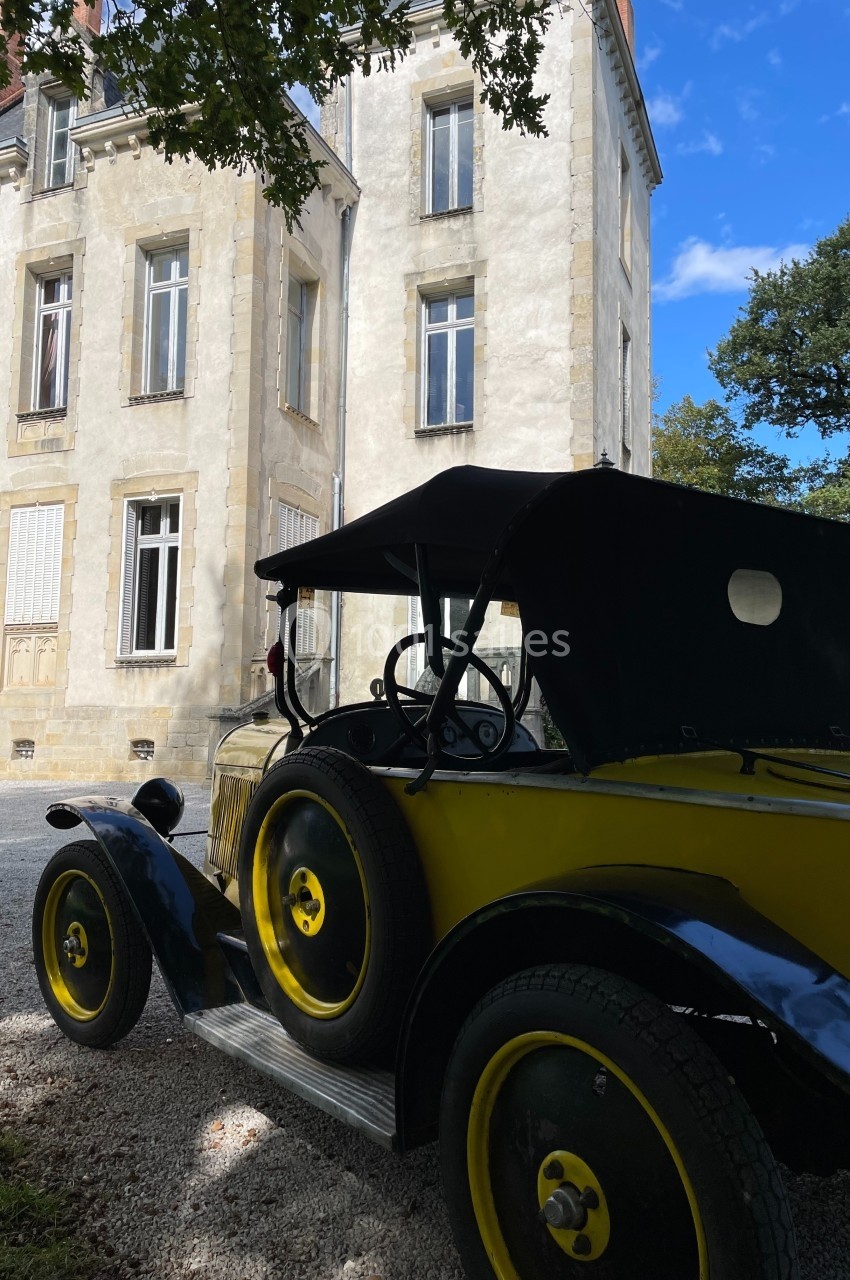 Voiture ancienne jaune et noire stationnée devant un bâtiment historique en pierre, sous un ciel partiellement dégagé.