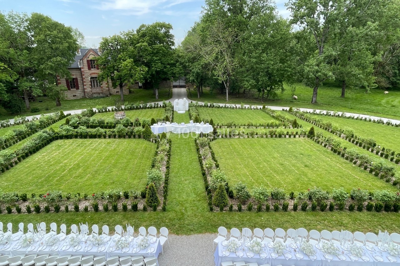 Jardin aménagé avec pelouses symétriques, tables dressées pour un événement en plein air et arbres en arrière-plan.