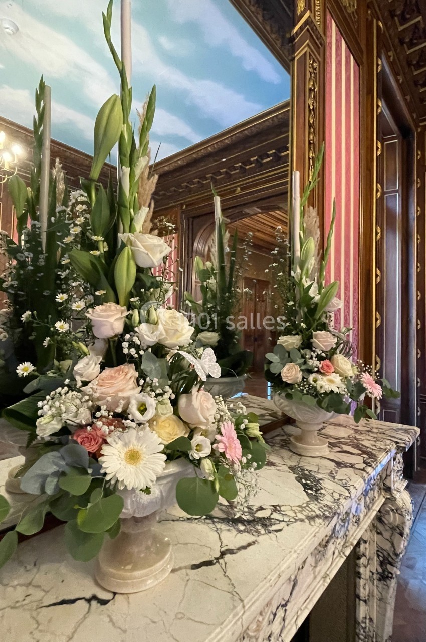 Arrangements floraux élégants avec roses et lys blancs sur une cheminée en marbre dans une pièce ornée de boiseries.