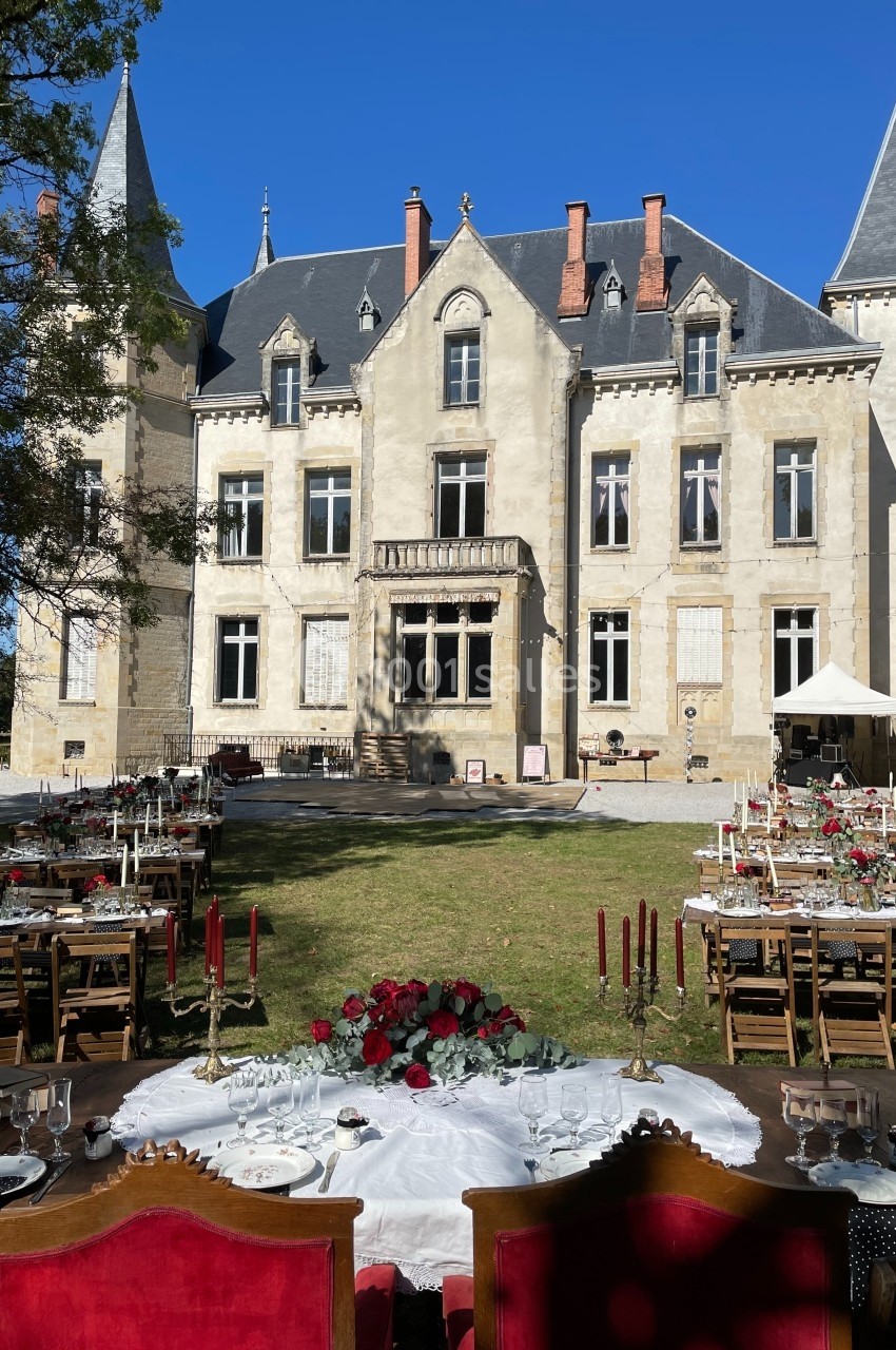 Tables décorées pour un événement en plein air devant un château avec tours et façade en pierre sous un ciel bleu.