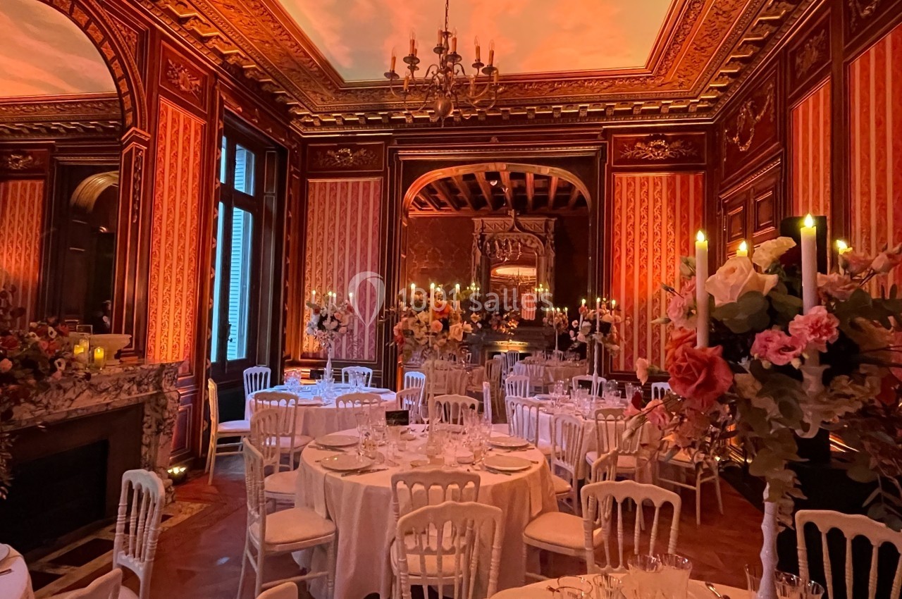 Salle de réception élégante avec tables dressées, chandeliers allumés et décorations florales dans un cadre boisé.