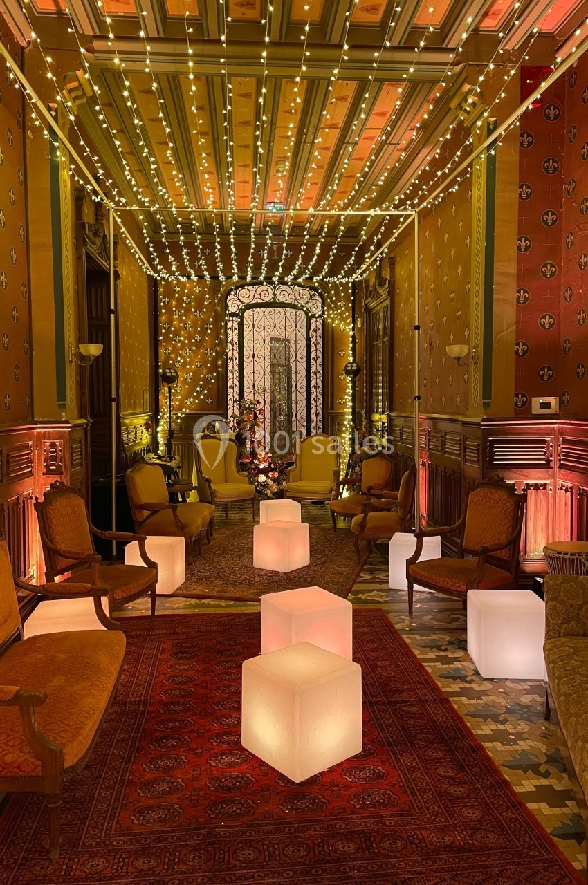 Salon décoré avec des guirlandes lumineuses, mobilier ancien et cubes lumineux sur un tapis rouge.