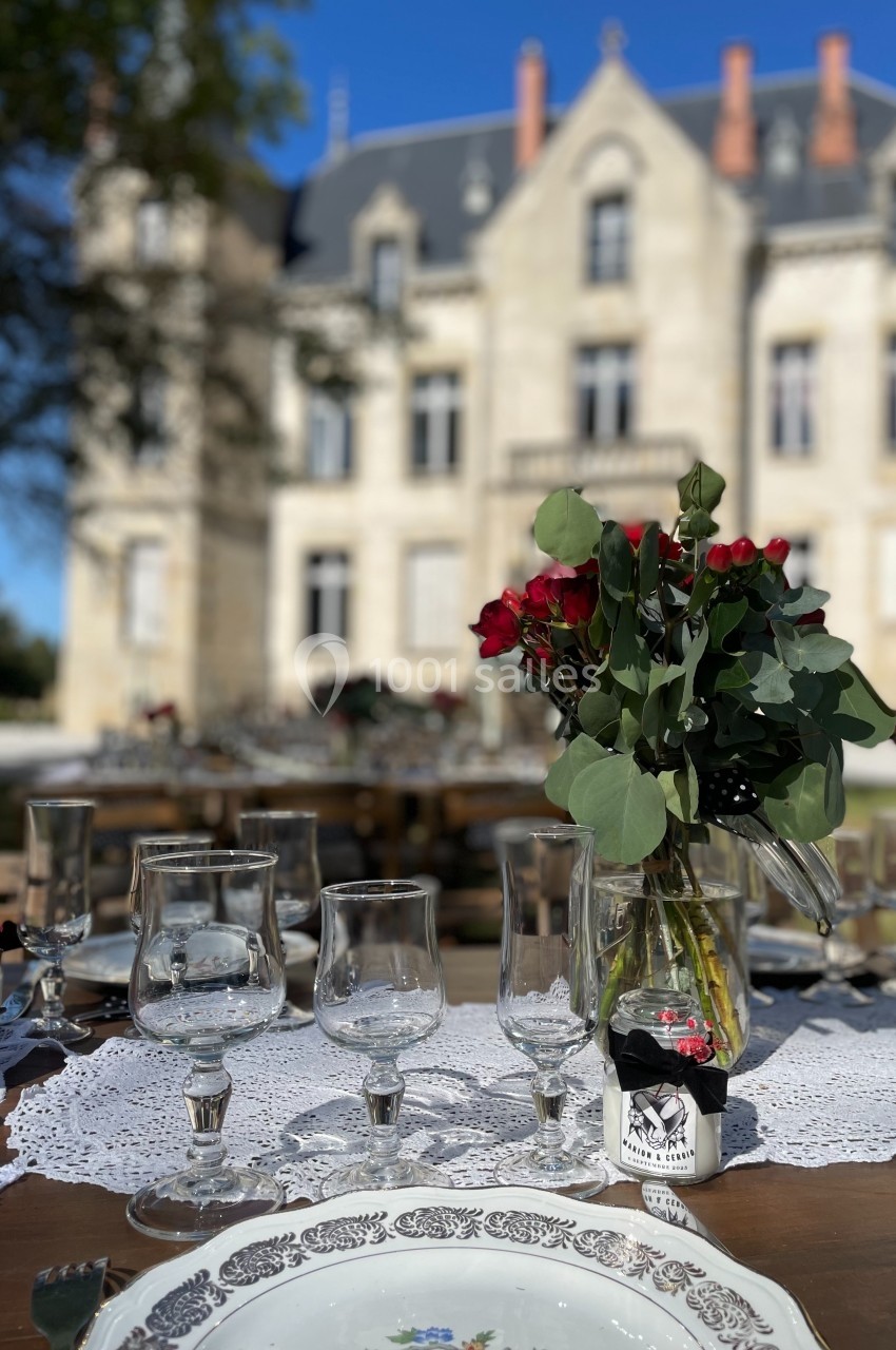 Table dressée avec vaisselle élégante et bouquet de roses rouges, devant un château en arrière-plan par temps ensoleillé.