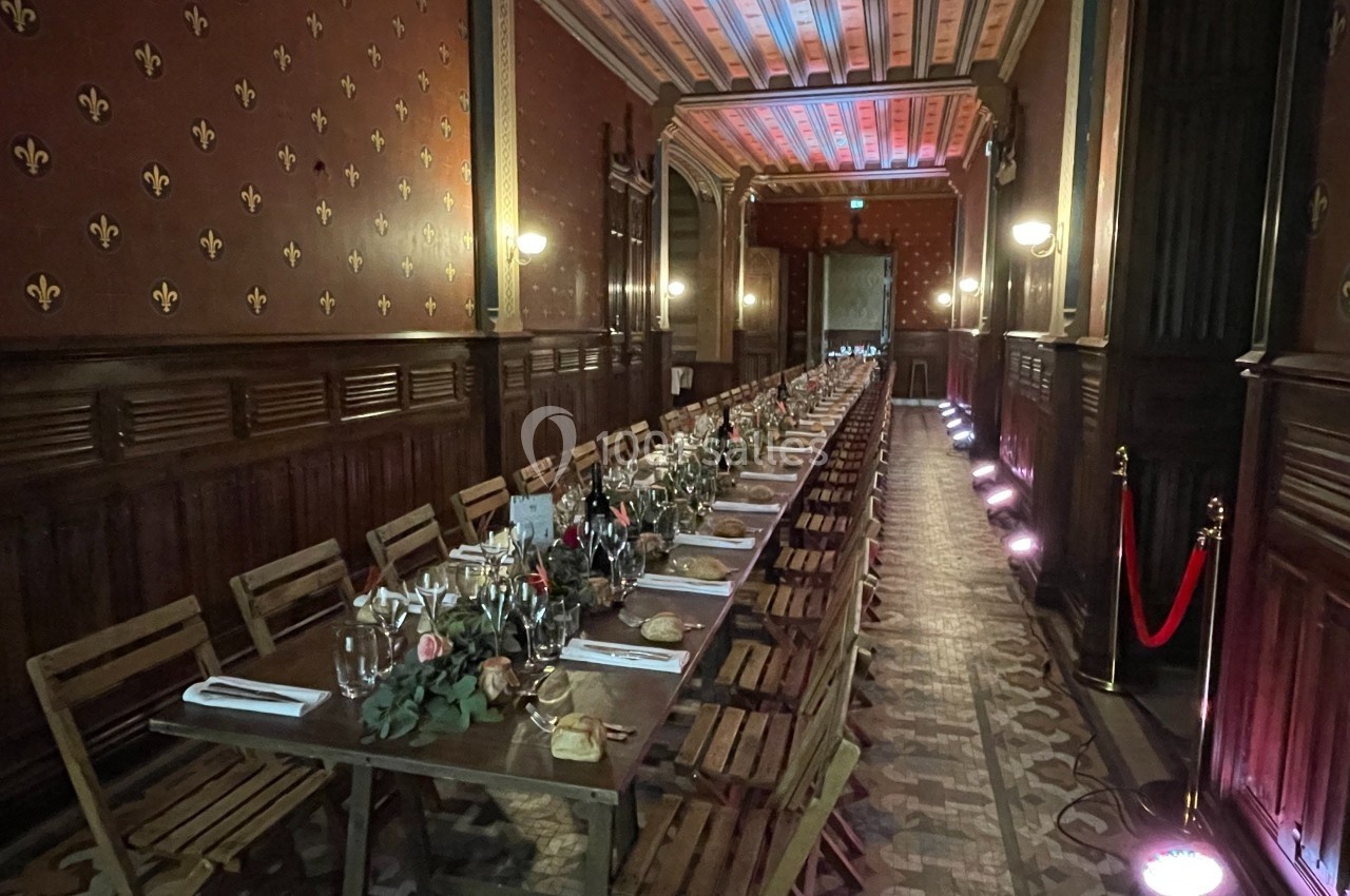 Grande table en bois dressée pour un repas dans une salle élégante avec murs ornés et éclairage tamisé.