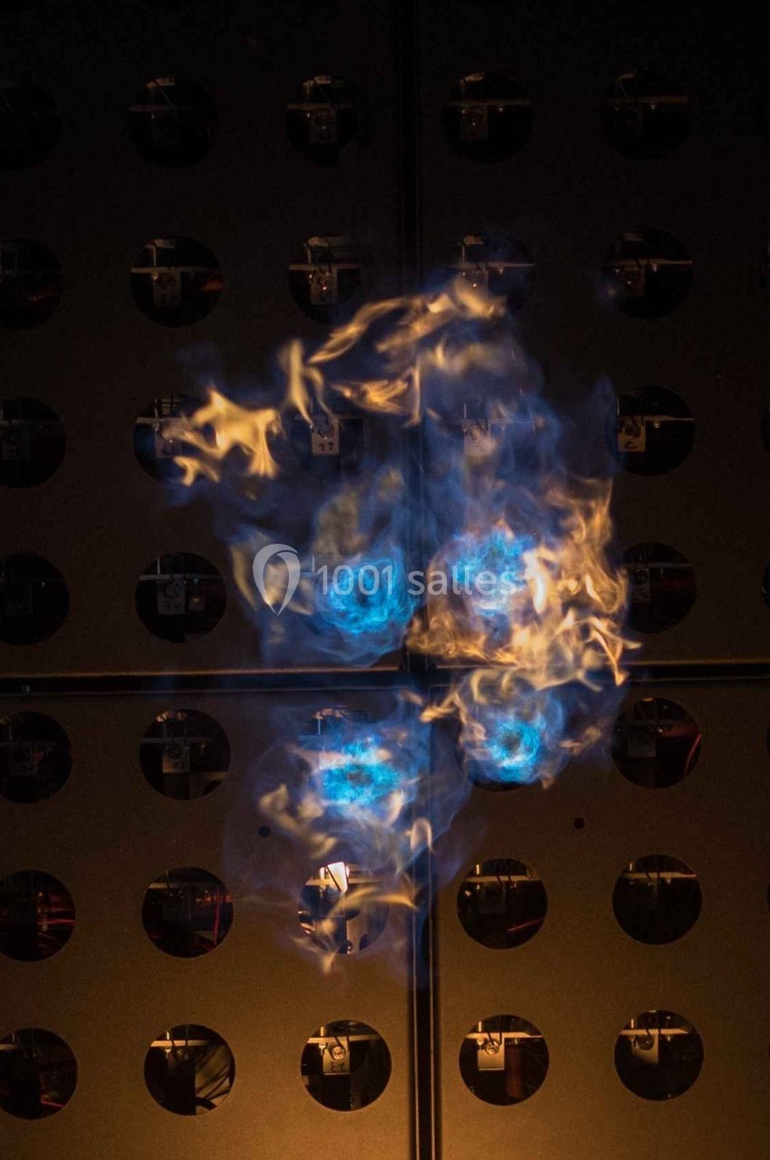 Flammes bleues et orange dans un environnement sombre avec un fond métallique perforé.