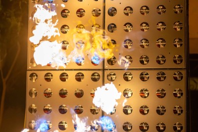 Colonnes de panneaux métalliques perforés émettant des flammes dans un environnement extérieur nocturne.