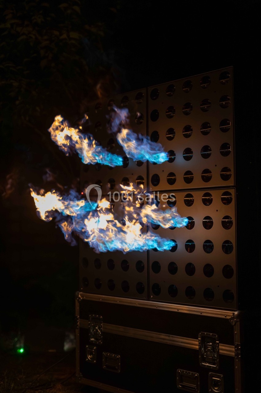Flammes bleues jaillissant d'une structure métallique perforée dans un environnement sombre.